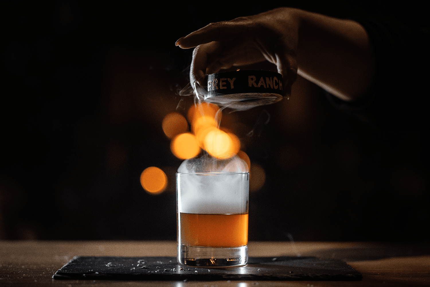 A close up shot of a hand holding a Frey Ranch puck over a glass of whiskey